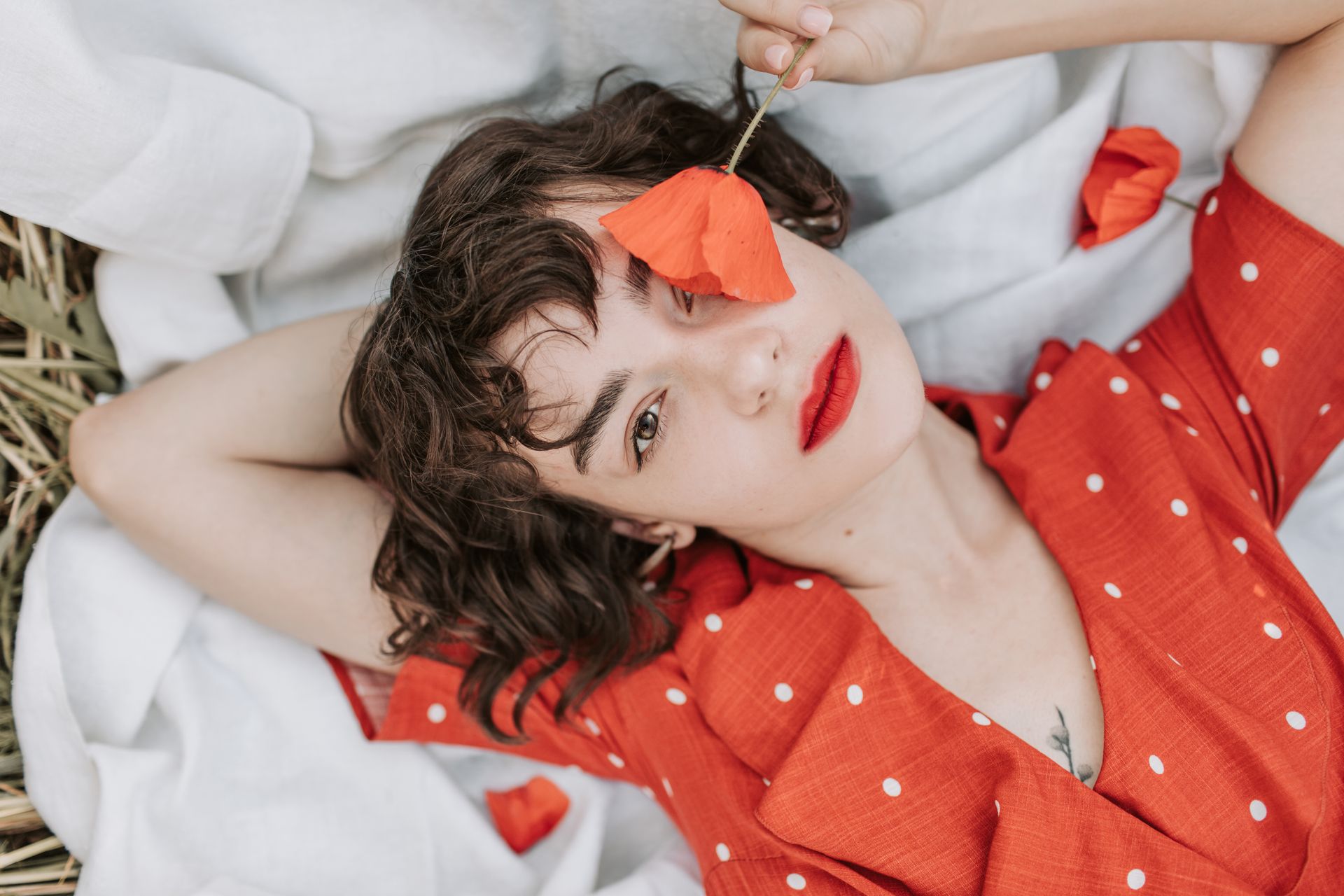 Woman in a Red and White Polka Dot Top Lying on White Textile