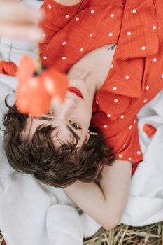 一名身穿橙色圆点连衣裙的女子，手拿一朵红花，躺在白色毯子上