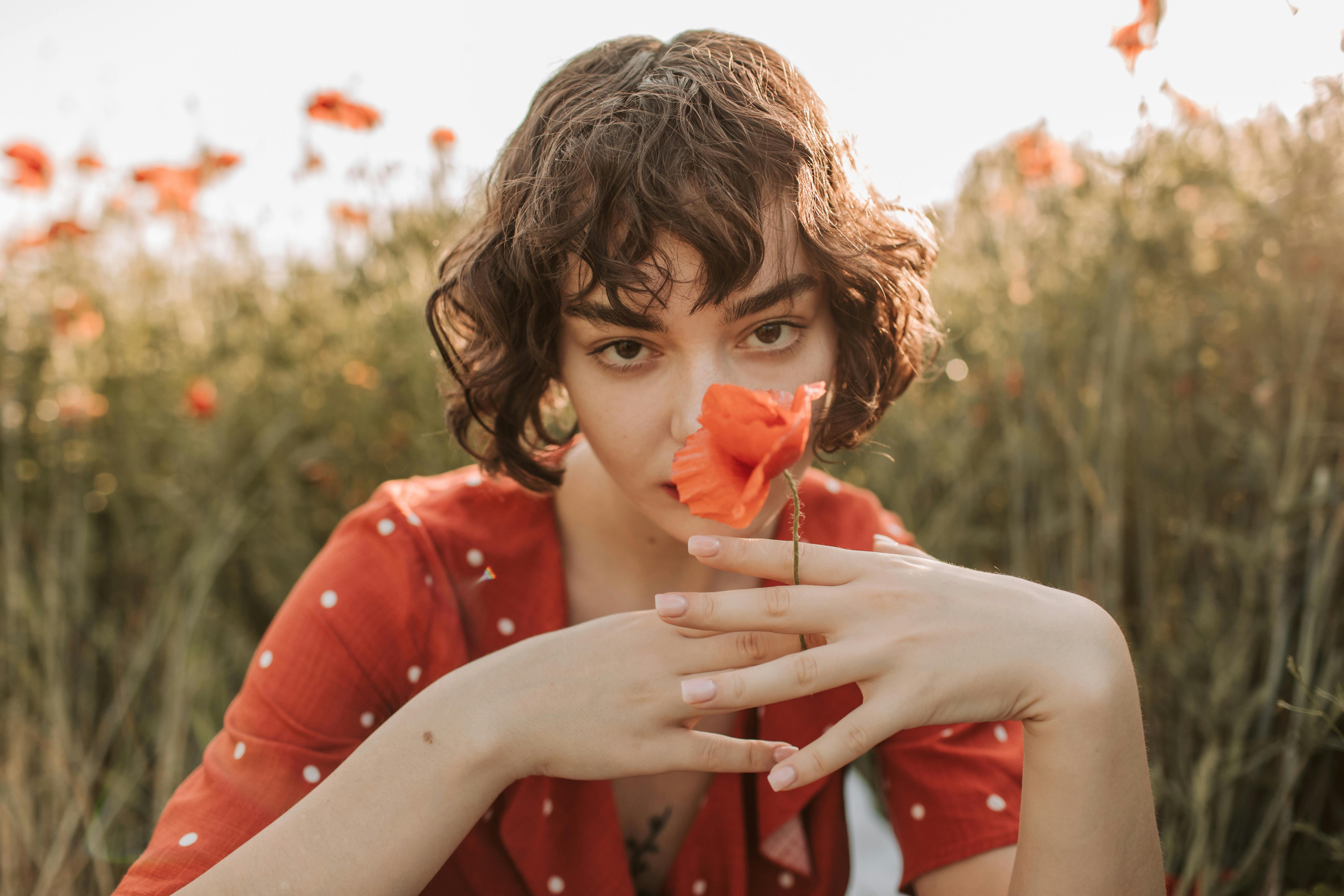 一名卷发女子身穿红色连衣裙，在阳光明媚的田野里手持罂粟花