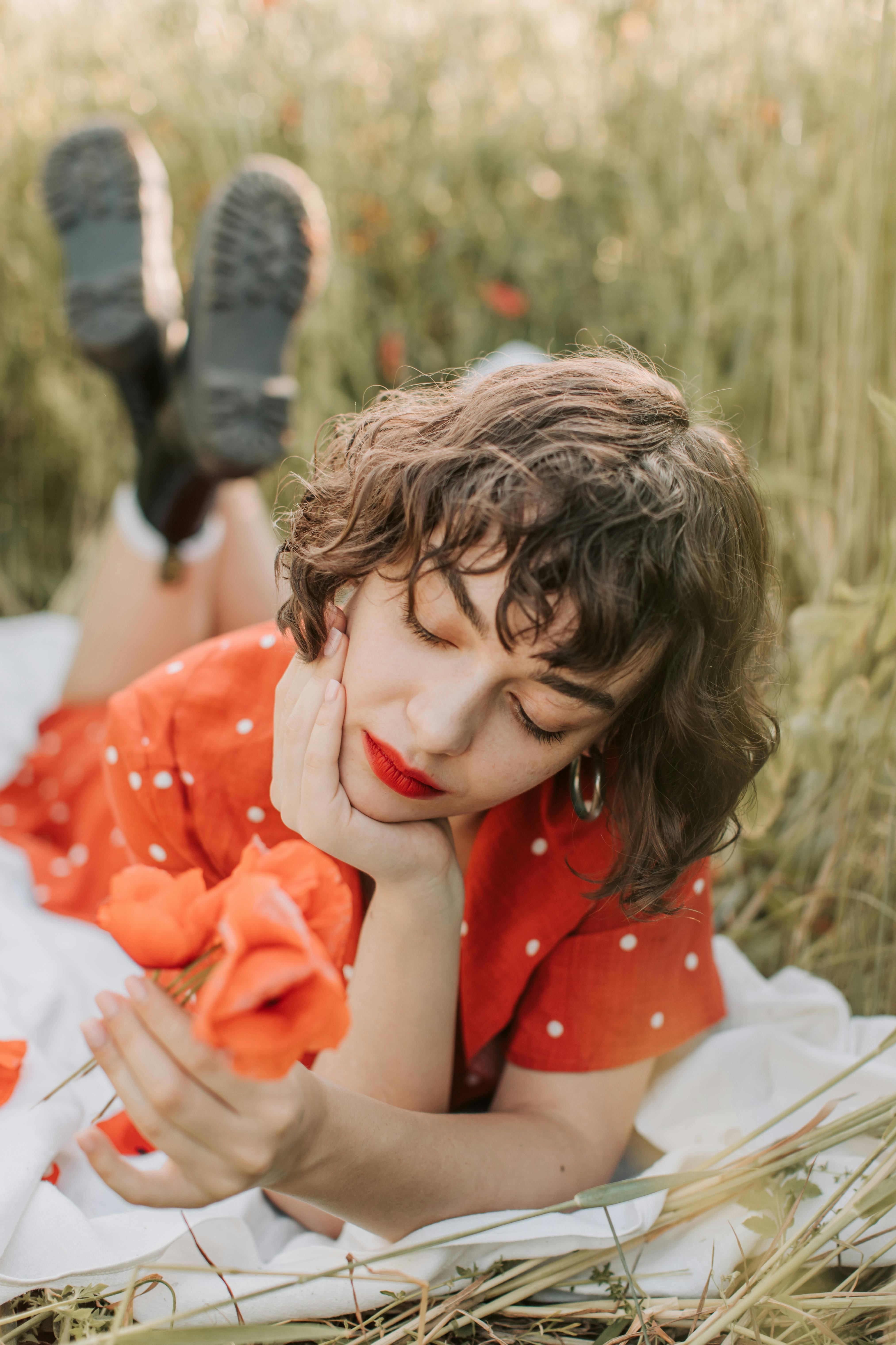 田野里，一名身穿红色连衣裙的女子手拿罂粟花躺在那里