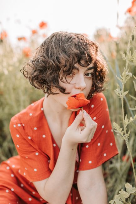 Young woman in a red polka dot dress sitting in a poppy field.