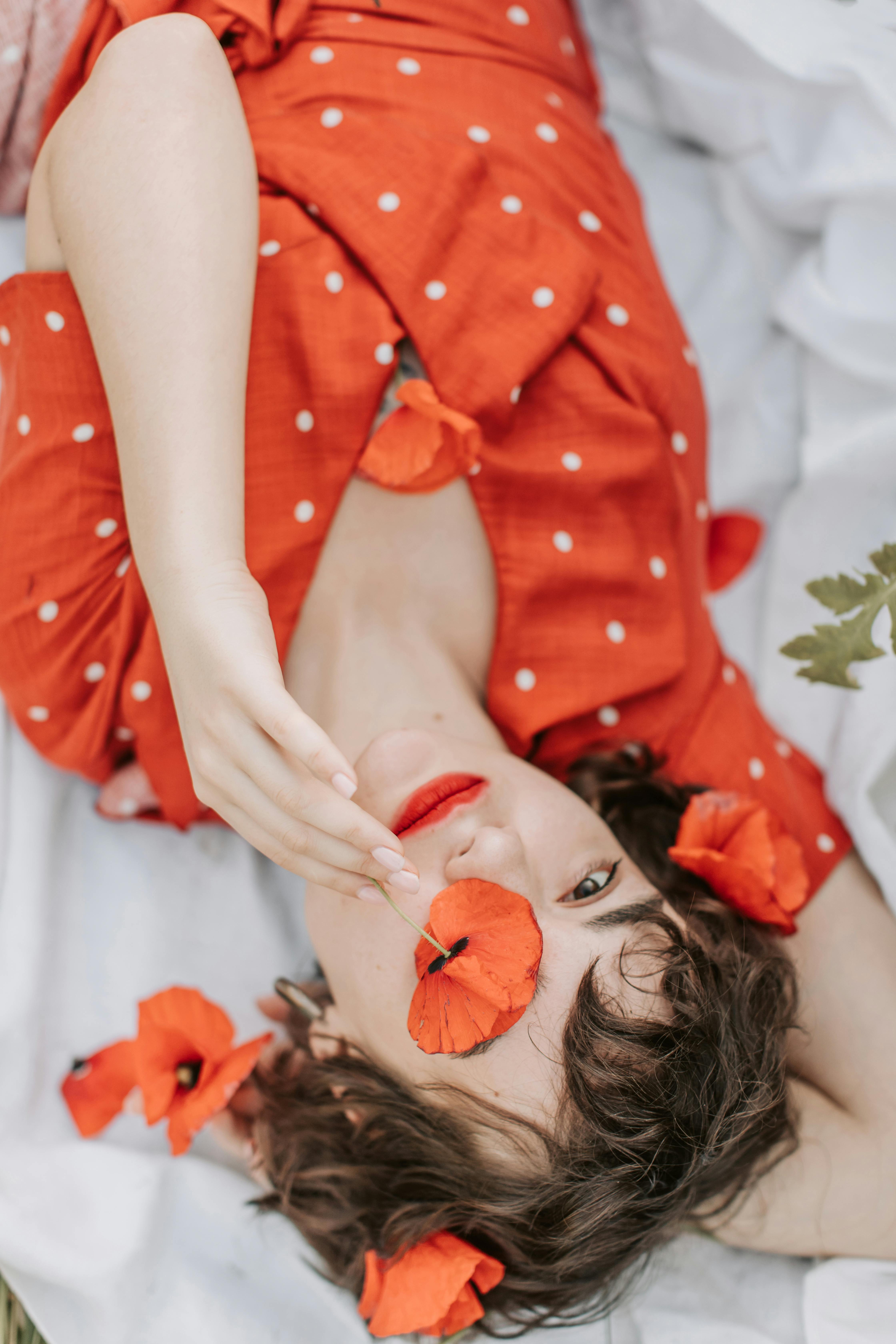 Woman in a red polka dot dress lying with poppy flowers, serene and artistic composition.