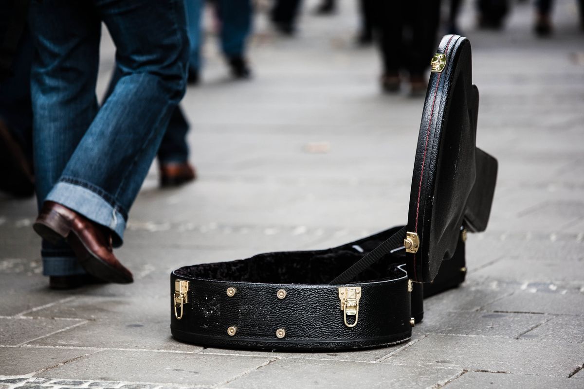 An open guitar case resting on a paved street during a busking session