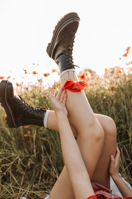 A woman relaxes in a poppy field, showcasing black boots and a carefree summer vibe.