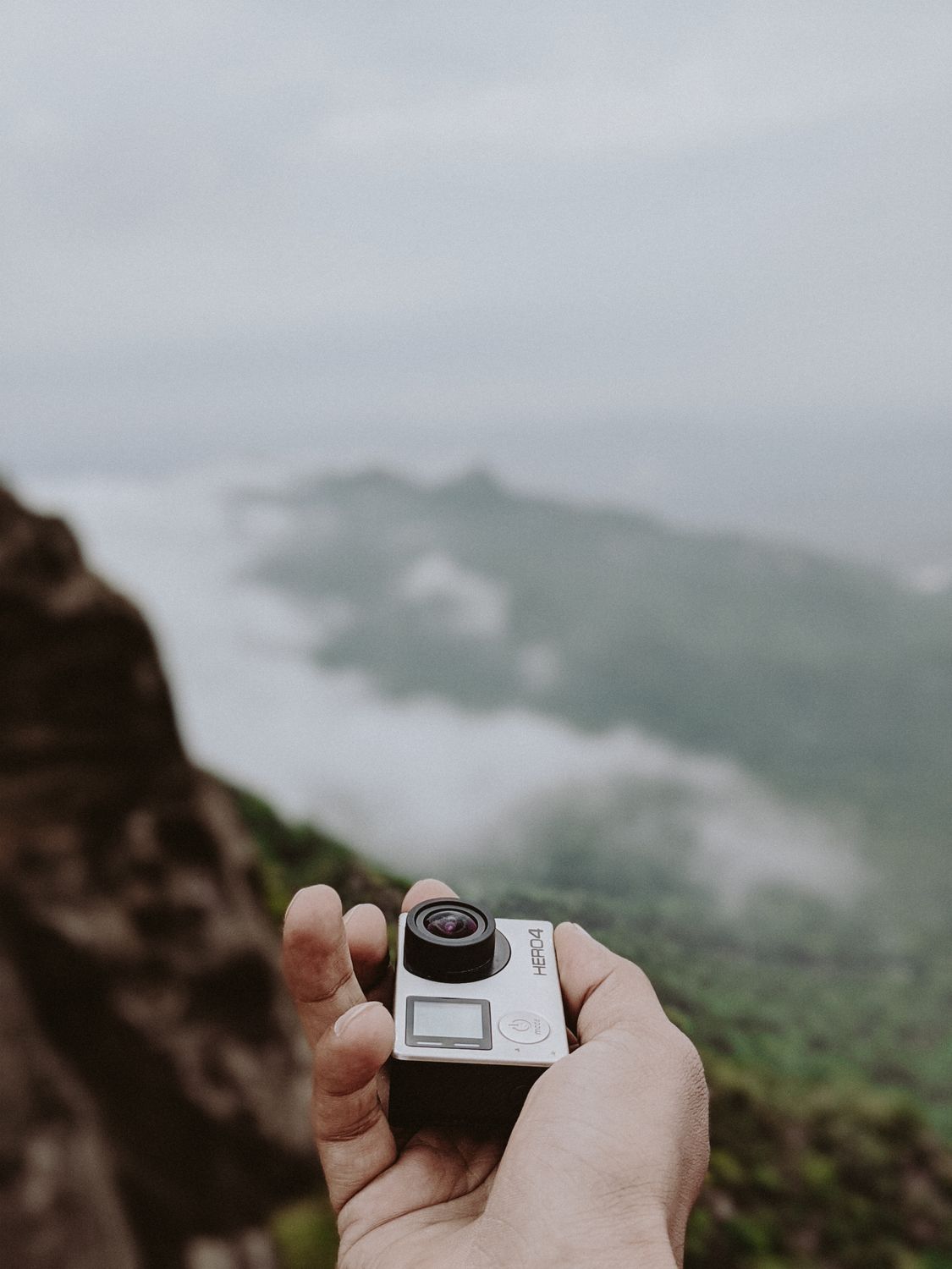 Hand holding an action camera against a misty mountain backdrop Hand holding an action camera against a misty mountain backdrop