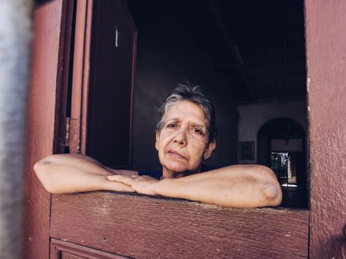 Free Senior female with short hair looking ar camera while leaning on wooden rack in doorway of house in daylight outside Stock Photo