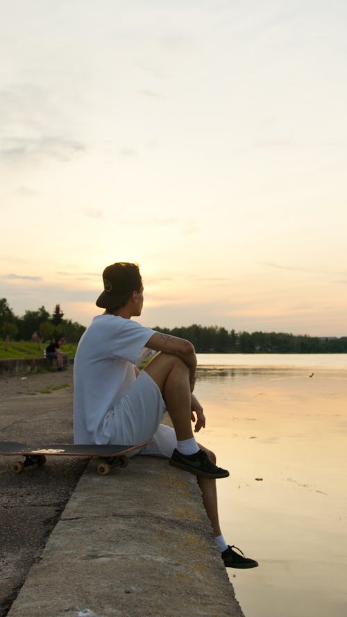 Man Sitting on Concrete Surface Beside his Skateboard 