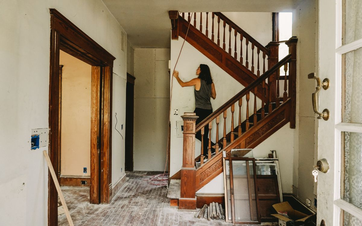 A woman working on home renovation featuring a wooden staircase.