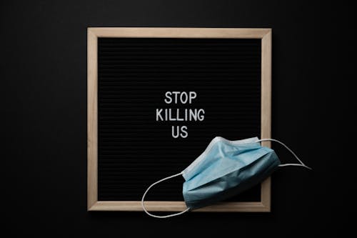 Top view of composition of blackboard with written phrase STOP KILLING US under mask against black background