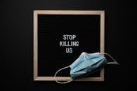 Top view of composition of blackboard with written phrase STOP KILLING US under mask against black background