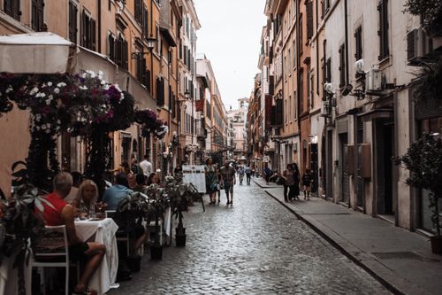 Free A bustling European cobblestone street lined with outdoor cafes and walking pedestrians. Stock Photo