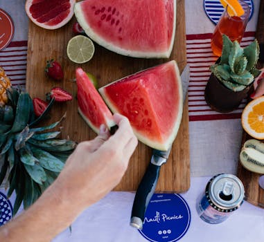 在充满活力的夏季野餐中，有新鲜切好的西瓜，并配有热带水果和清凉饮料