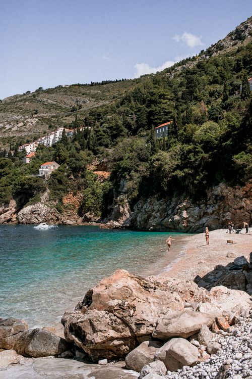 Free Picturesque beach scene with rocky shore and lush hills, perfect for a tranquil getaway. Stock Photo