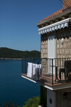 Stone balcony with laundry and scenic view of blue sea and distant greenery under clear sky.