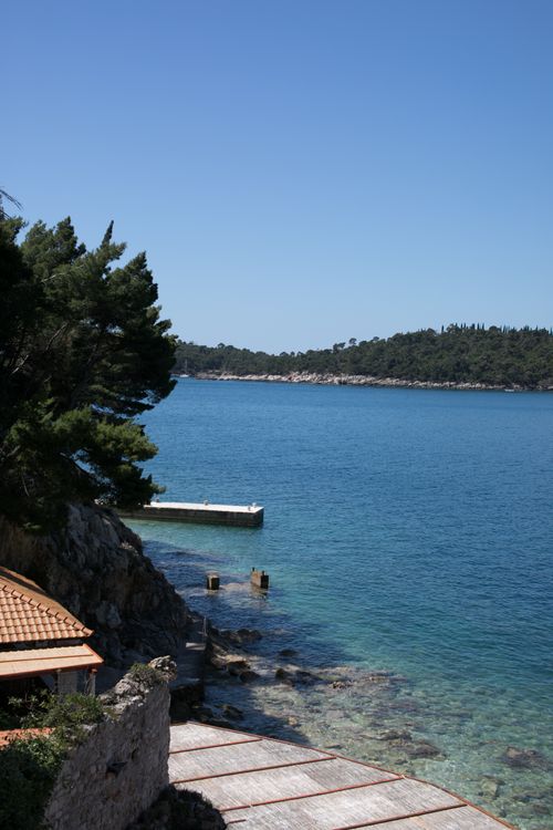 Free A tranquil coastal scene with clear blue waters and sky, surrounded by lush greenery. Stock Photo