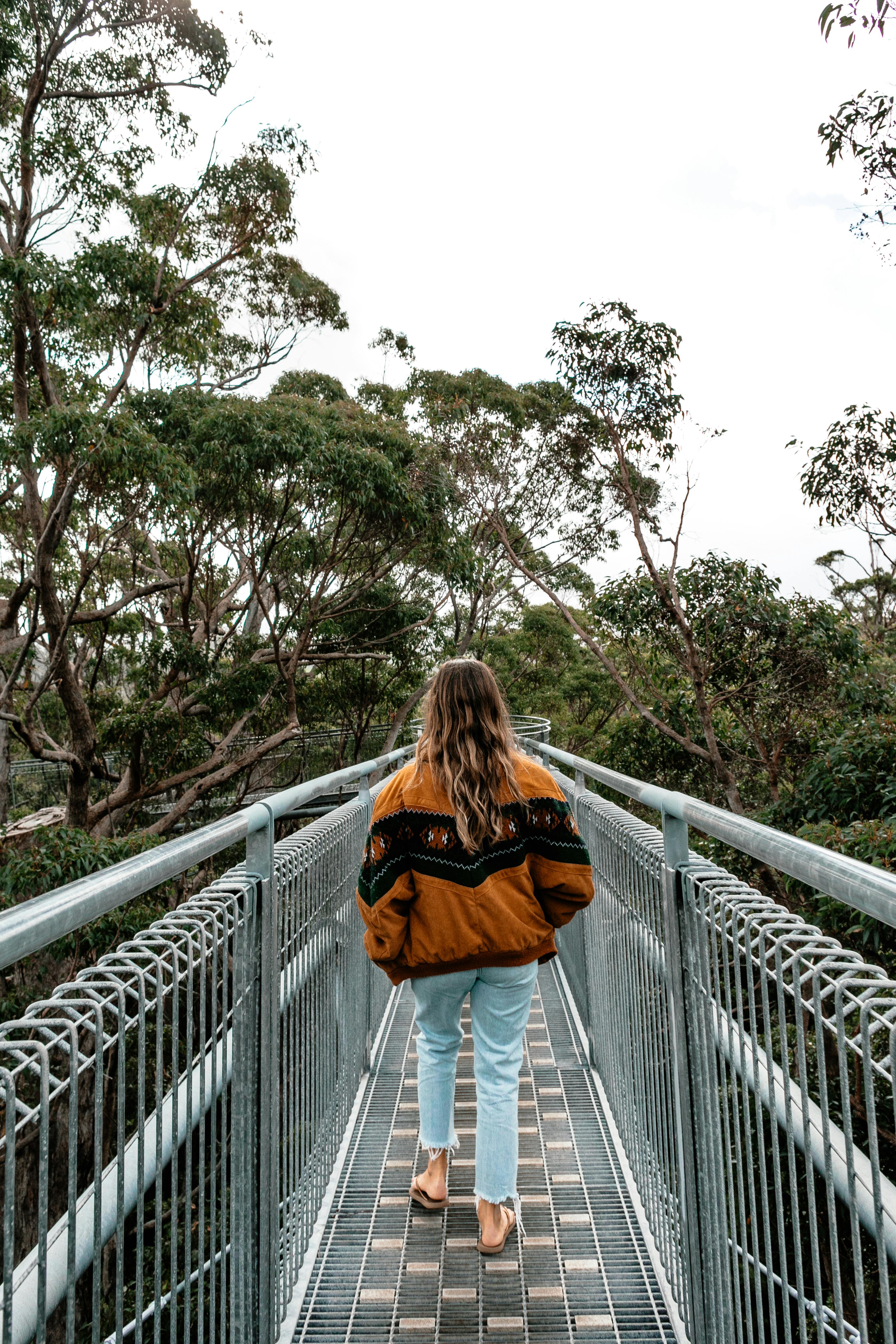一名妇女穿着夹克，走在树木环绕的高架桥上