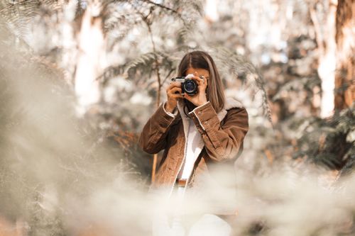 Free A woman in a brown coat captures nature's beauty with her camera. Stock Photo