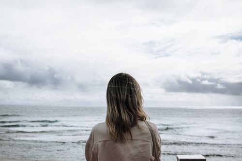 Free Woman with blonde hair looking at the ocean under a cloudy sky, creating a serene and contemplative setting. Stock Photo