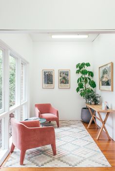Bright, minimalist reading nook featuring pink armchairs, leafy plants, and modern artwork.