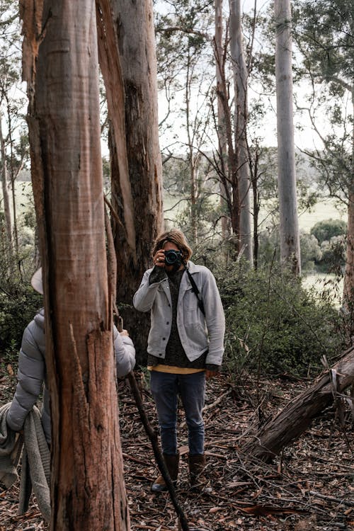 Man in Gray Jacket and Denim Jeans Standing Beside Tree While Taking Picture 