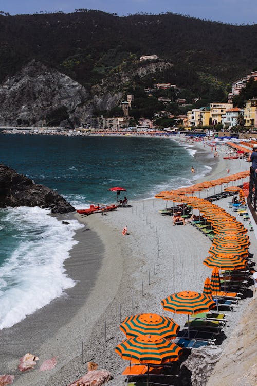 Amazing view of sandy beach with bright umbrellas and loungers and foamy water against rocky mountains