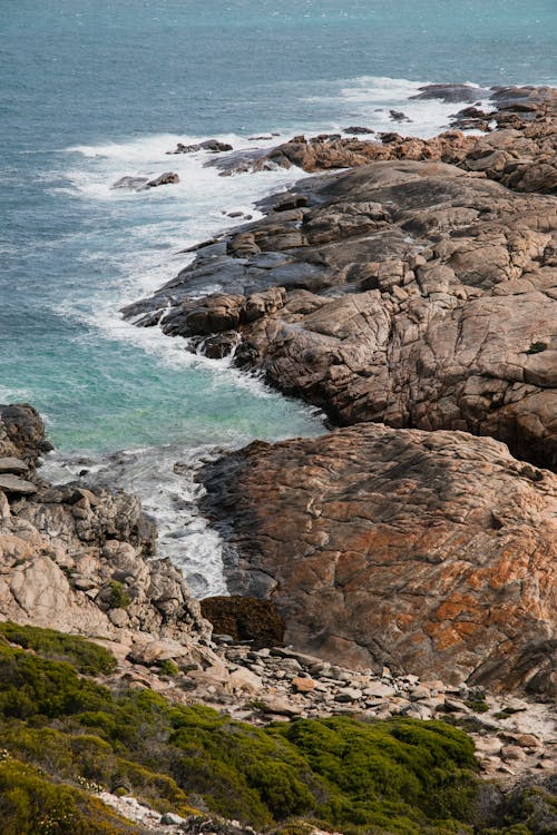 Rough rocky coast partly covered with moss of sea with light blue transparent water and foamy waves