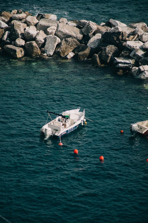 From above of small motorboat floating on sea with blue water near pile of rough rocks