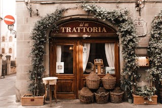 Exterior of cozy Italian restaurant with wooden door and entrance decorated with plants