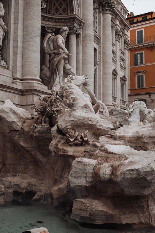 Famous old stone statues decorating large fountain located near old buildings in Rome