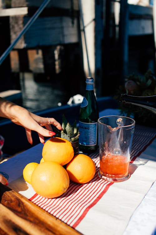 Crop unrecognizable female taking ripe fresh orange and drink in bottle to make alcoholic cocktail