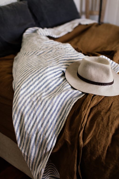 Free White stylish hat on blanket with stripes on unmade comfortable bed in bedroom Stock Photo