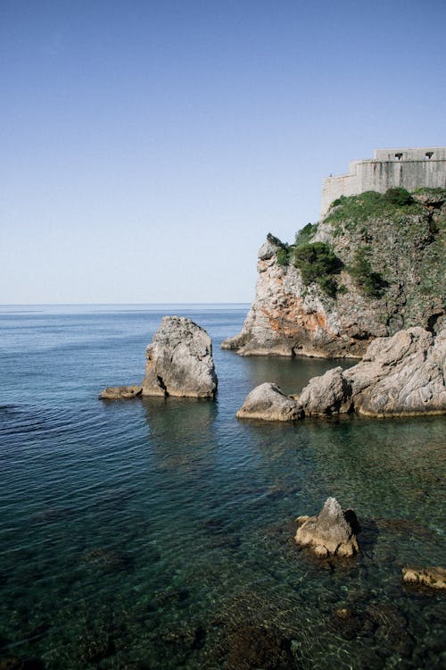 Picturesque view of rough rocky cliff with green grass near calm blue sea water