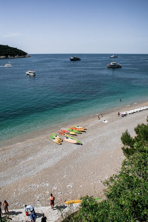 Picturesque view of turquoise wavy sea water near sandy beach with tourists and surfboards