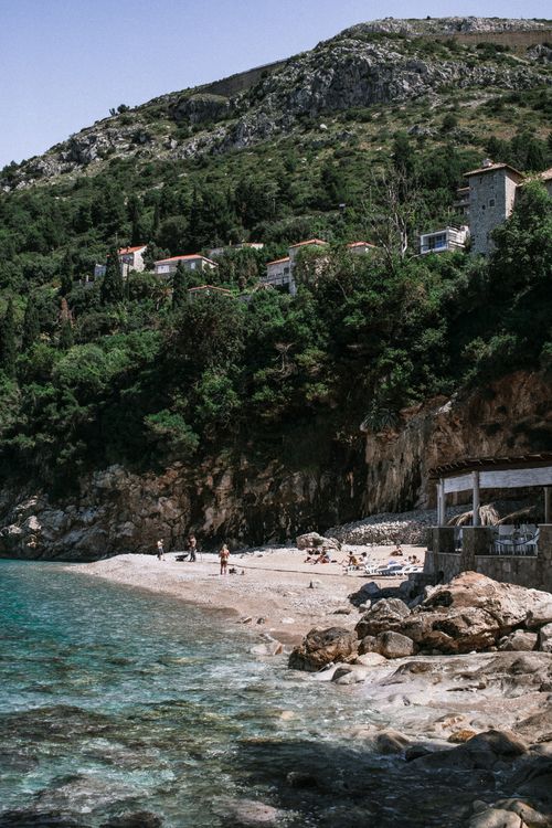 Free People resting on sandy shore with rocks near rippling blue sea water against mountain Stock Photo