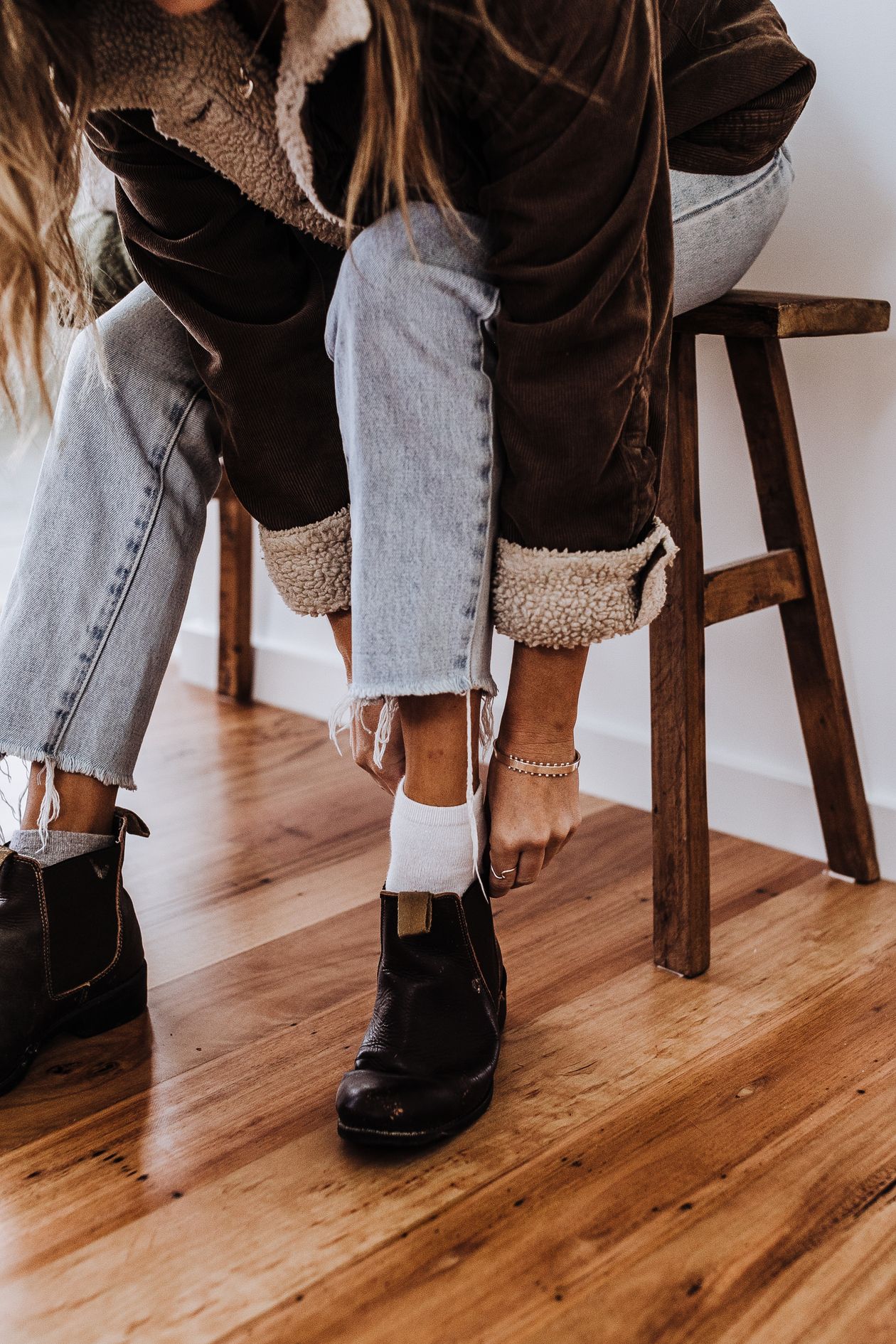 Woman pulling on dark brown chelsea boots with cropped frayed jeans