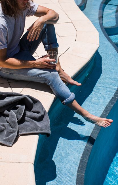 Man relaxing by the poolside with a wine glass, enjoying a sunny day.