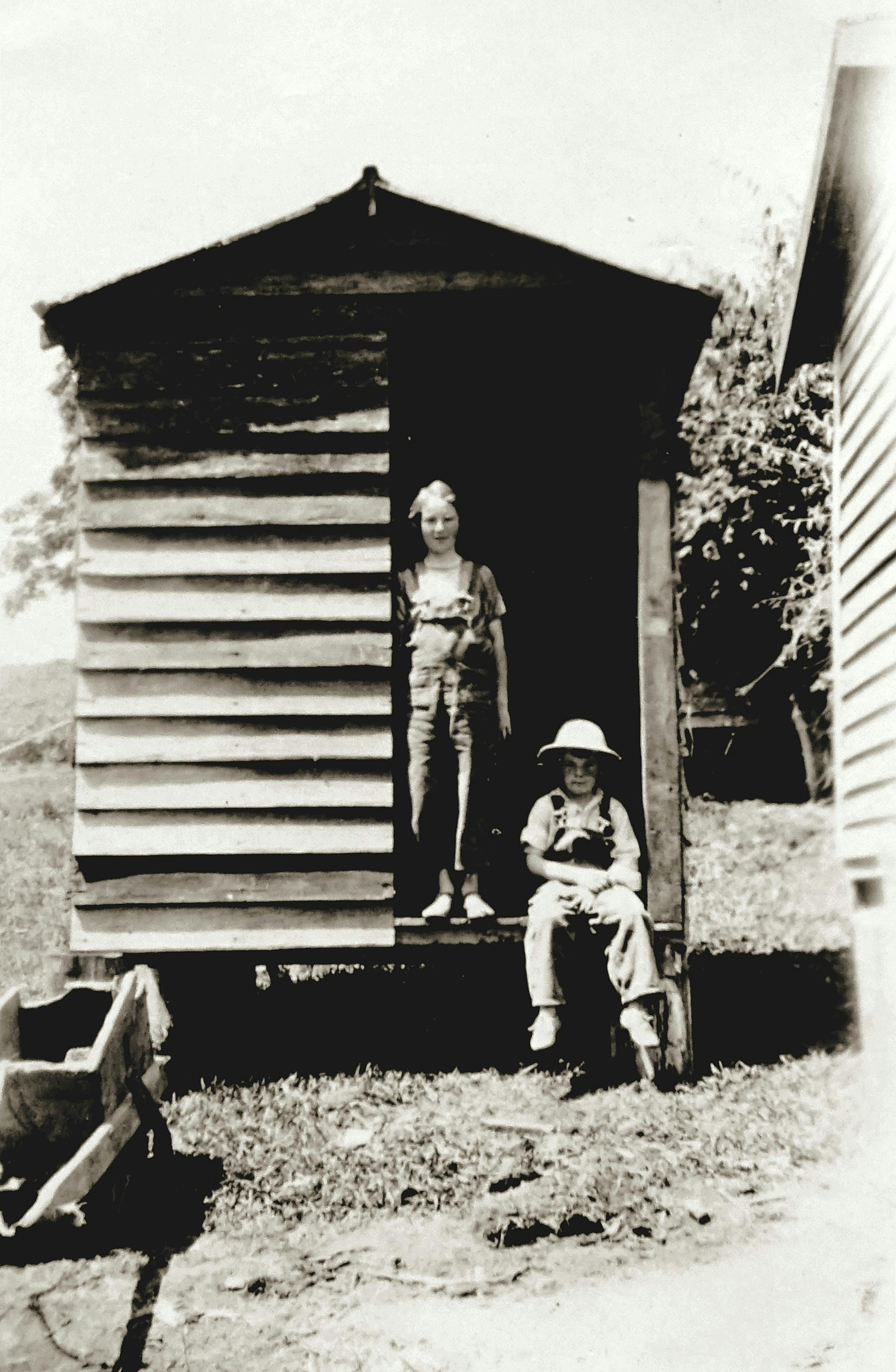 Old fashioned photo of two children standing at a rustic cabin, capturing nostalgia.