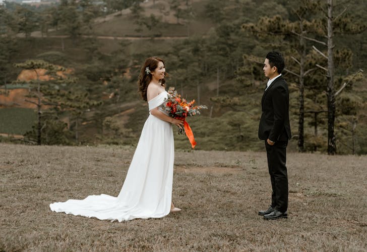Happy Asian bride and groom standing on grassy ground