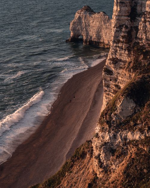 Free Stunning seascape of Étretat's iconic cliffs and coastline in warm sunset light. Stock Photo