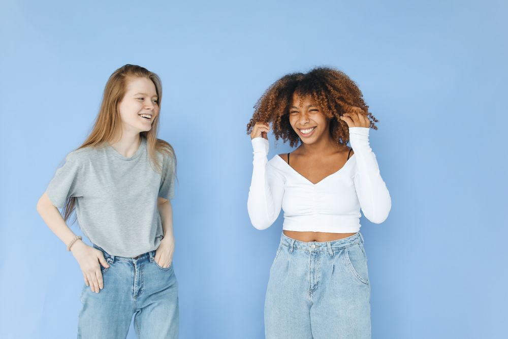 Photo by Polina Tankilevitch on Pexels — two colleagues laughing against a blue backdrop