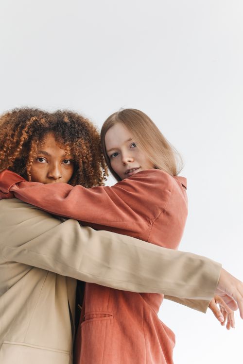 Free Portrait of two women hugging in elegant coats, symbolizing friendship and diversity. Stock Photo