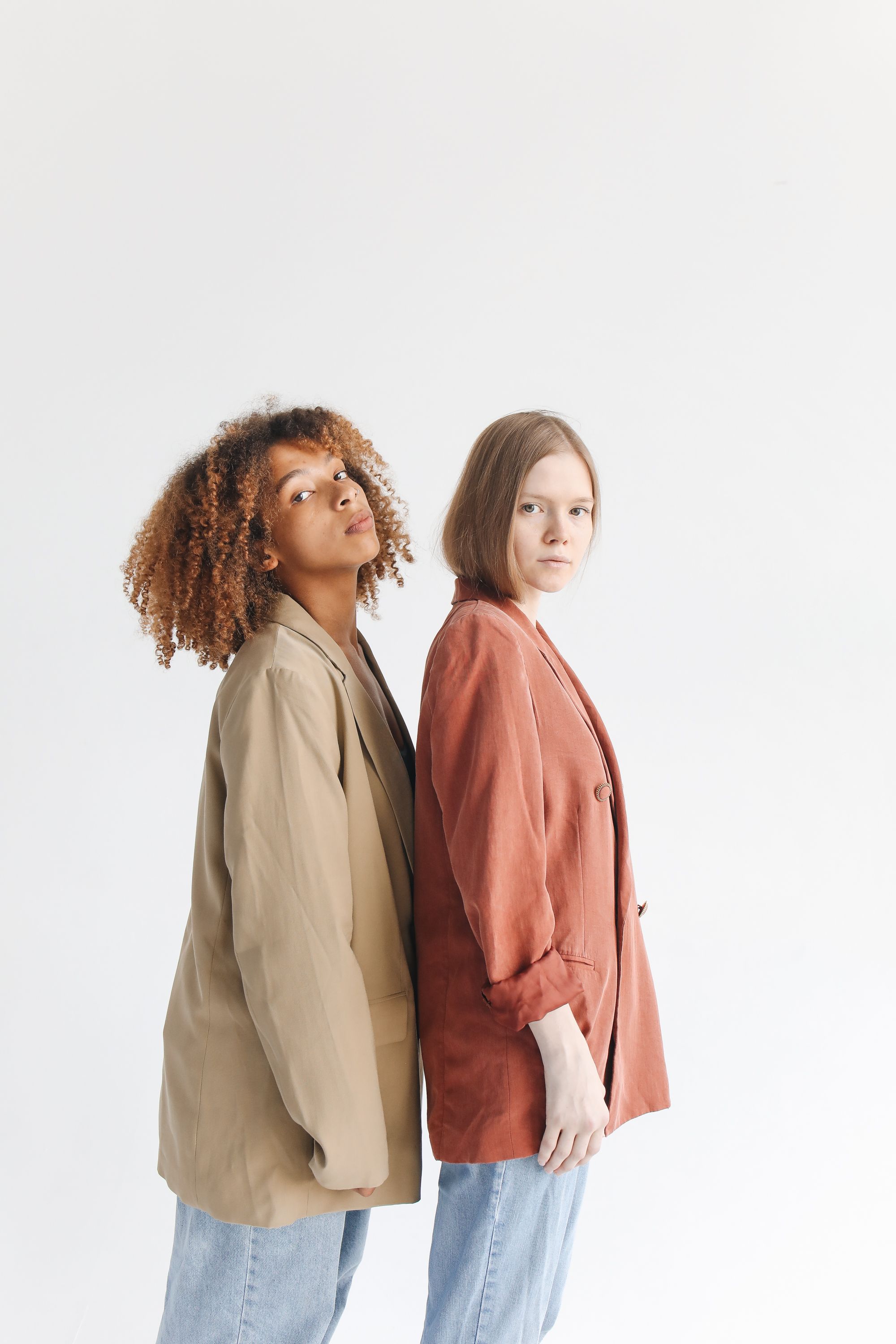 Duas jovens mulheres fashion posando de costas uma para a outra em um estúdio.