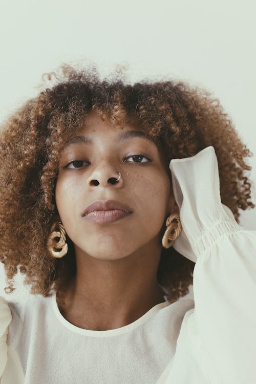 Free Close-up portrait of a woman with afro hair wearing a white top and stylish earrings. Stock Photo