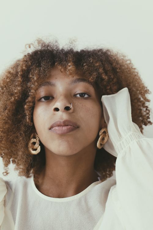 Free Close-up portrait of a woman with afro hair wearing a white top and stylish earrings. Stock Photo
