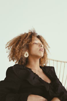 Elegant portrait of a woman with curly hair and hoop earrings against a light background.