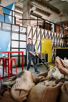 一名穿着制服的男子正在现代工业仓库里操作手推车，仓库里堆放着咖啡袋