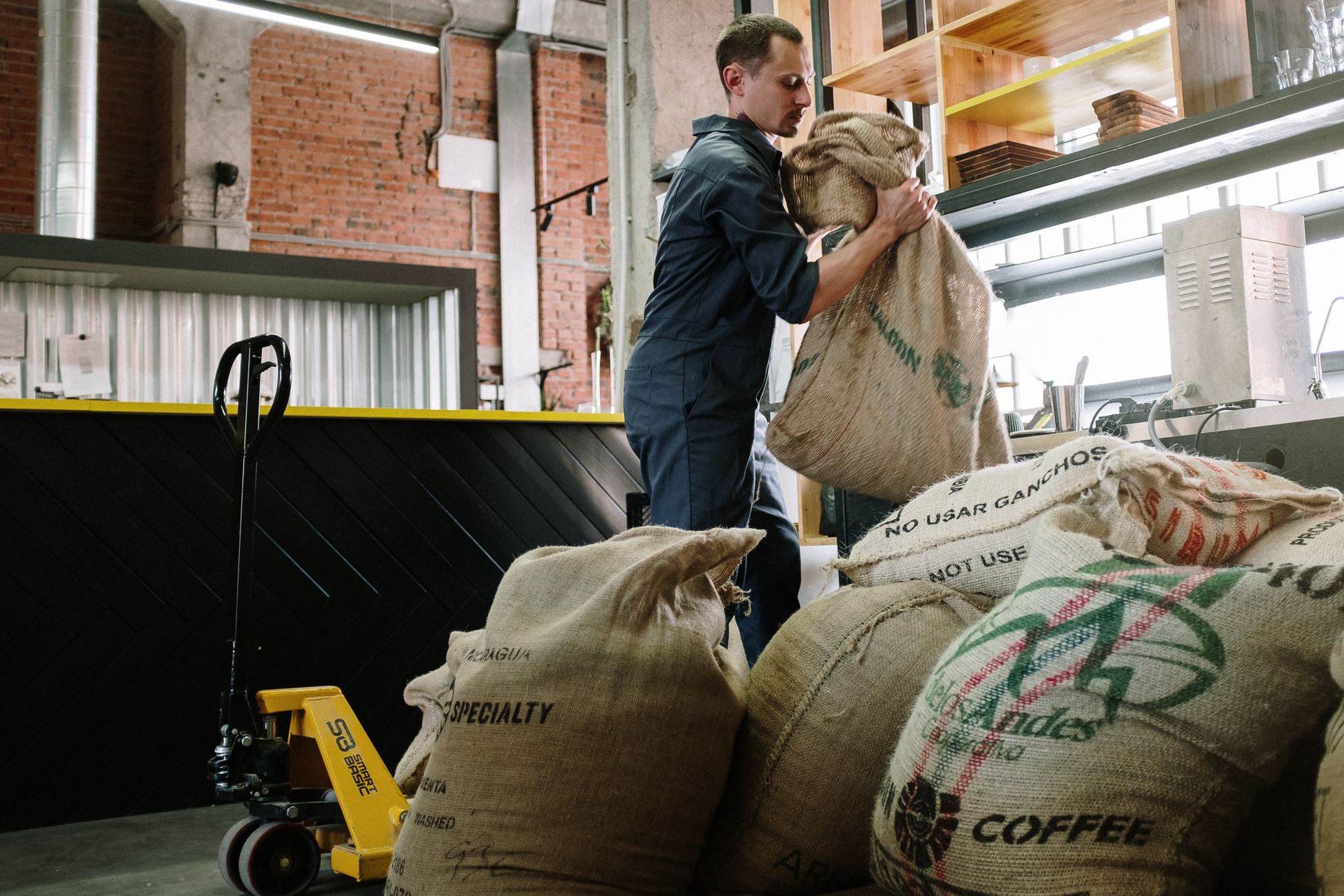 Warehouse employee handling burlap coffee sacks, industrial setting.