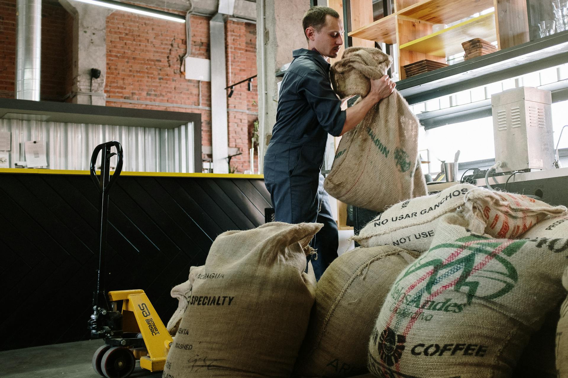 Warehouse employee handling burlap coffee sacks, industrial setting.