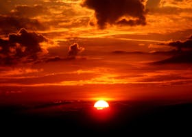 Vivid sunset with a glowing sun on the horizon and dramatic clouds, casting warm tones.