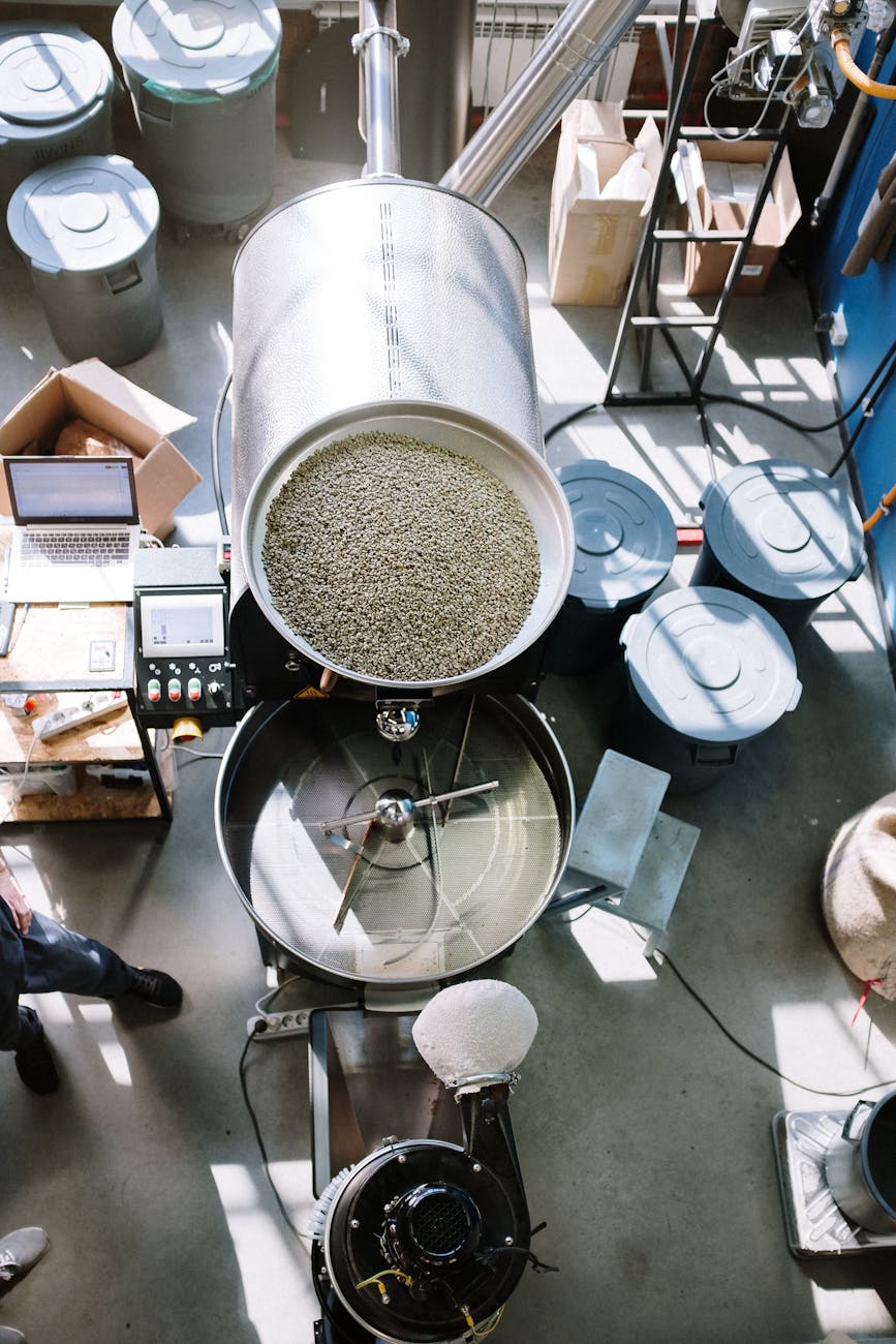 overhead view of industrial coffee roaster with raw beans in a workshop setting.